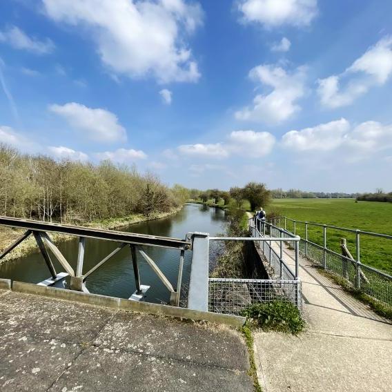 Riverbank and bridge beside a field.